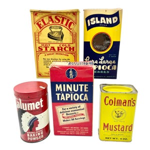 May include: A collection of vintage food packaging, including boxes of starch, tapioca, and mustard. The packaging features bold colors and retro graphics, such as an iron on the starch box and a Native American figure on the baking powder can.
