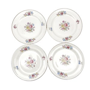 May include: Set of four white ceramic dinner plates with a gold rim and floral design. Each plate features a different arrangement of pink, yellow, and blue flowers.