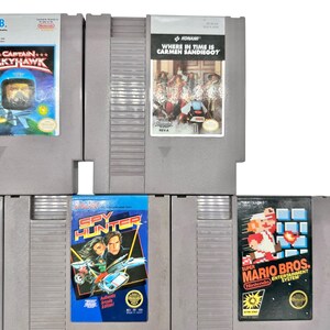 Pode incluir: Uma cole&ccedil;&atilde;o de cartuchos de jogos vintage para o Nintendo Entertainment System (NES). Os t&iacute;tulos incluem "Captain Skyhawk", "Where in Time is Carmen Sandiego?", "Spy Hunter" e "Super Mario Bros.". Os cartuchos s&atilde;o cinzentos com r&oacute;tulos de jogos coloridos.