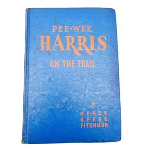 Puede incluir: Un libro antiguo titulado "Pee-Wee Harris on the Trail" de Percy Keese Fitzhugh. El libro tiene una cubierta azul con letras naranjas. La cubierta muestra signos de desgaste, lo que sugiere su antigüedad.
