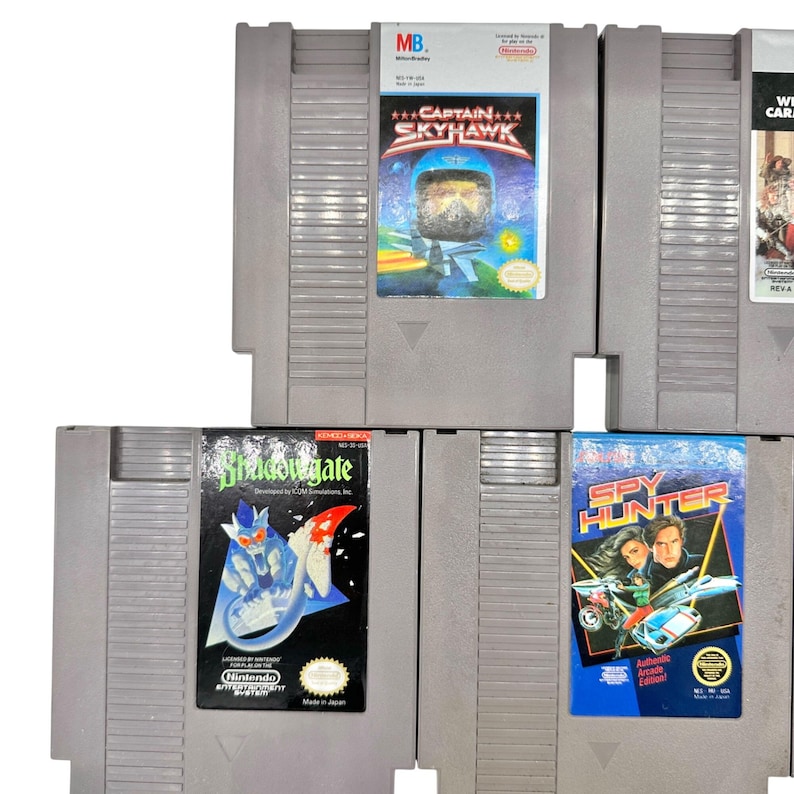 Pode incluir: Uma cole&ccedil;&atilde;o de cartuchos de jogos Nintendo Entertainment System (NES) vintage. Os cartuchos cinzentos apresentam r&oacute;tulos coloridos com t&iacute;tulos de jogos como "Captain Skyhawk", "Shadowgate" e "Spy Hunter". Os r&oacute;tulos mostram temas de a&ccedil;&atilde;o e aventura.