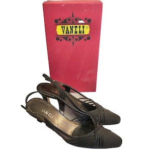 Puede incluir: Un par de tacones negros de tiras con un diseño tejido. Los zapatos están sobre una caja roja con el nombre de la marca "Vanelli" impreso en ella.