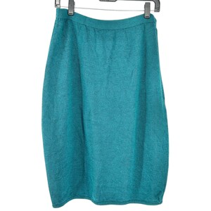 May include: Teal-coloured knitted skirt hanging on a black hanger. The skirt is a solid colour and appears to be made of a soft, textured material. The skirt is knee-length and has a straight silhouette.