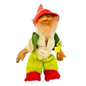 May include: A vintage gnome doll with a red hat, green vest, and yellow pants. The doll has a smiling face, a white beard, and a tag that says "Lucki". The doll's red boots complete the whimsical look.