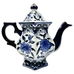 Könnte beinhalten: Eine weiß-blaue Keramik-Teekanne mit floralem Design. Die Teekanne hat einen dunkelblauen Griff, Ausguss und Akzente. Der Deckel ist mit einem kleinen Knauf versehen. Die Teekanne ist etwa 20 cm hoch.