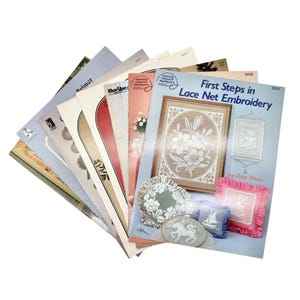 May include: A collection of vintage embroidery books, including "First Steps in Lace Net Embroidery" by Rita Weiss. The covers feature floral designs, lace patterns, and illustrations in various colors. The books are fanned out, showcasing their titles and artwork.