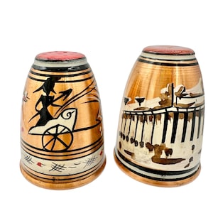 May include: A pair of copper-toned salt and pepper shakers with hand-painted designs. One depicts a chariot scene, the other a building. Each has a red top and black stripes, with a height of approximately 7 cm.