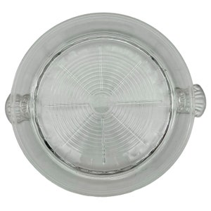 May include: A clear glass cake plate with a raised, circular design and two handles. The plate has a textured surface and is designed to hold a cake or other dessert.