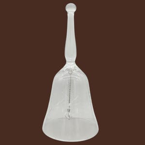 Könnte beinhalten: Eine Glocke aus klarem Glas mit einem langen, schlanken Griff und einem ausgestellten Körper. Die Glasoberfläche ist mit zarten, geätzten Blumenmustern verziert. Eine dünne, silberfarbene Metallkette hängt im Inneren und endet in einem Klöppel.