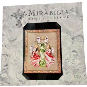 May include: Cross-stitch pattern featuring three fairies with wings, wearing pink and green dresses, holding a cup and a flower. The pattern is titled "Mirabilia cross-stitch" and is priced at $11.00.