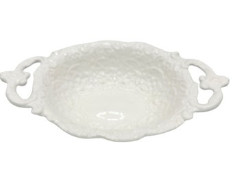 May include: White ceramic serving bowl with two ornate handles. The bowl has a textured, embossed design.