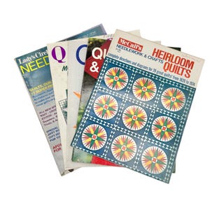May include: A stack of vintage quilting and needlework magazines. The top magazine features a blue cover with a grid of colorful starburst patterns. Other magazines include titles like "Lady's Circle Needles" and "Quilts".