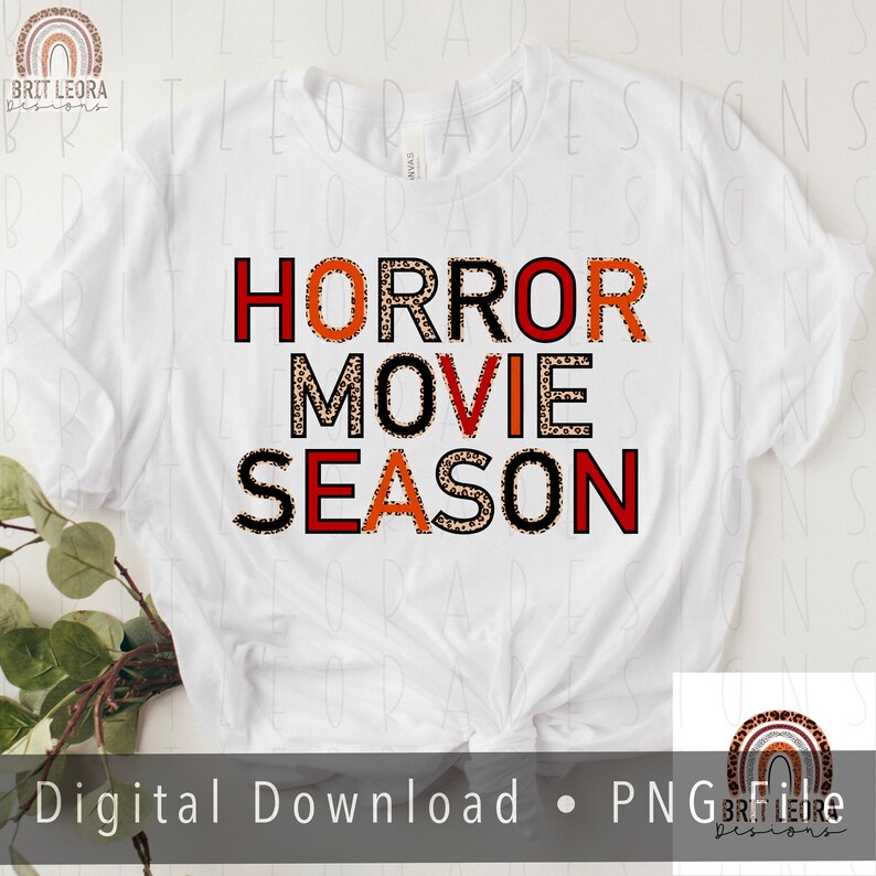 May include: White t-shirt with the text "HORROR MOVIE SEASON" in black letters with a leopard print pattern. The letters are outlined in red.