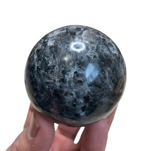 May include: A black and grey labradorite sphere with a smooth, polished surface. The sphere is about 2 inches in diameter and has a unique, iridescent sheen.