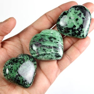 May include: Three green and black heart-shaped stones with a polished finish. The stones have a mottled pattern of green, black, and white.