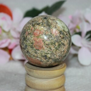 May include: A green, pink and white speckled sphere made of polished stone, resting on a wooden stand.