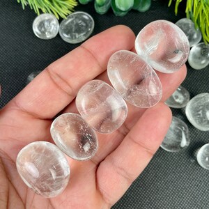 May include: A collection of smooth, clear quartz crystal stones, also known as clear quartz, in various sizes and shapes. The stones are tumbled and polished, with a smooth, glassy finish.