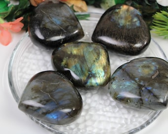 May include: Five heart-shaped labradorite stones in shades of black, blue, and green with iridescent shimmer. The stones are arranged on a white, textured surface.