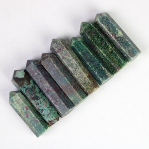 Op de afbeelding: Een set van negen groene, grijze en paarse edelsteenstaven, gerangschikt in een rij, met de punten naar rechts wijzend.