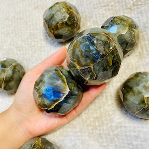 May include: Six faceted labradorite spheres in various shades of green, blue, and grey. The spheres are arranged in a cluster, with some of them overlapping.
