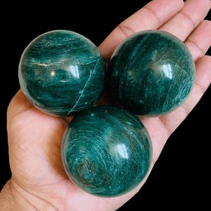Peut inclure: Trois sphères lisses, vertes et polies d'aventurine, une variété de quartz, avec des motifs tourbillonnants. Les sphères sont présentées dans une main.