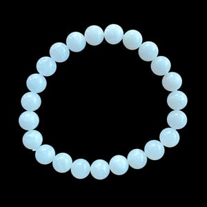 Puede incluir: Un brazalete blanco hecho de cuentas redondas y lisas. El brazalete mide aproximadamente 18 cm de largo.