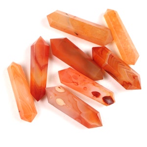 May include: A group of seven carnelian crystal points, each with a unique orange and white banded pattern. The points are arranged in a random pattern on a white background.