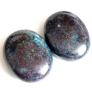 May include: Two smooth, oval-shaped stones with a dark blue, green, and brown marbled pattern. The stones have a glossy finish.