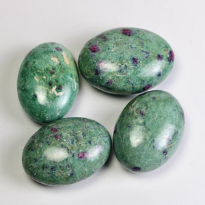 May include: Four oval stones with a green base colour and small red inclusions. The stones have a smooth, polished surface and are arranged on a white background. The stones appear to be gemstones or decorative rocks.