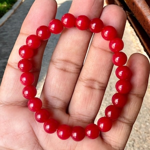 May include: A red beaded bracelet with round beads. The bracelet is made of smooth, polished stones.