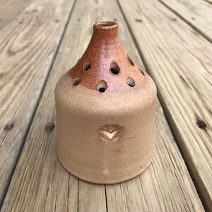 May include: A small, brown ceramic vase with a flared top and a decorative design. The vase has multiple holes around the top for holding flowers.