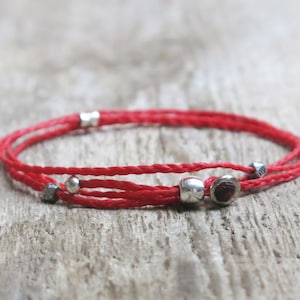 Könnte beinhalten: Rotes Armband mit silbernen Perlen und einem kleinen roten Edelstein.