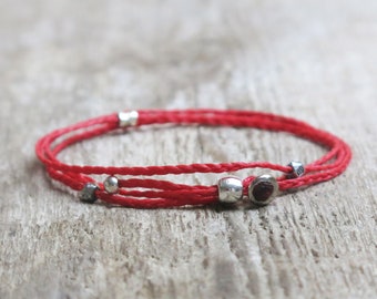 Op de afbeelding: Rood koord armband met zilveren kralen en een kleine rode edelsteen.