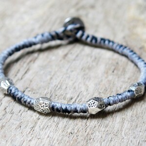 Può includere: Un braccialetto intrecciato grigio e nero con perline in metallo argentato. Il braccialetto ha un design semplice ed è un ottimo accessorio per qualsiasi outfit.