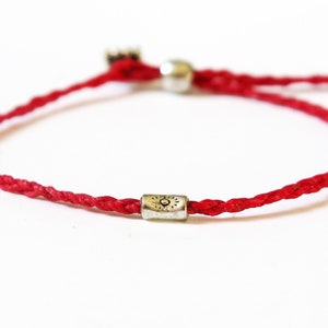 May include: A red string bracelet with a silver charm featuring a sun symbol.