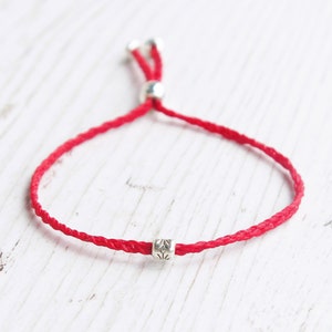 Könnte beinhalten: Ein rotes Armband aus Schnur mit silbernen Perlen. Das Armband ist mit einem Schiebeknoten verstellbar.