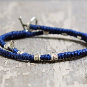 Op de afbeelding: Een gevlochten armband in marineblauw met zilveren accenten. De armband heeft een sluiting.