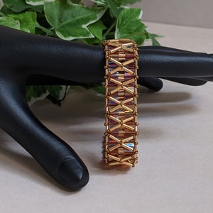 Könnte beinhalten: Ein goldenes Armband mit schillernden Glasperlen. Das Armband ist mit einem gewebten Muster gefertigt.