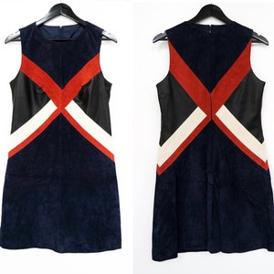 K&ouml;nnte beinhalten: &Auml;rmelloses marineblaues Kleid mit geometrischem Design. Das Kleid hat rote, schwarze und wei&szlig;e Akzente. Das Kleid h&auml;ngt an einem schwarzen Kleiderb&uuml;gel. Das Kleid ist aus Wildleder und Leder.