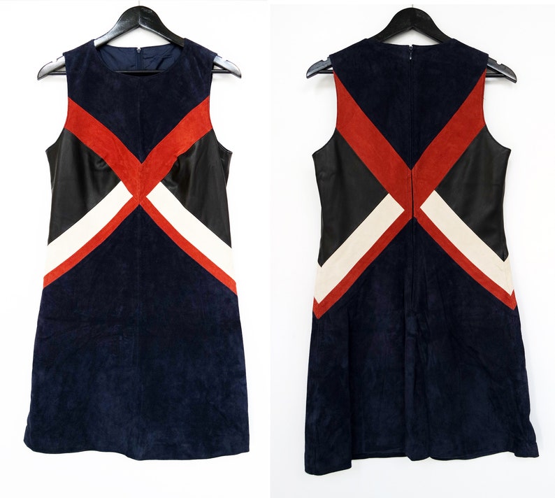 K&ouml;nnte beinhalten: &Auml;rmelloses marineblaues Kleid mit geometrischem Design. Das Kleid hat rote, schwarze und wei&szlig;e Akzente. Das Kleid h&auml;ngt an einem schwarzen Kleiderb&uuml;gel. Das Kleid ist aus Wildleder und Leder.