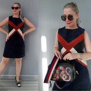 K&ouml;nnte beinhalten: &Auml;rmelloses marineblaues Kleid mit einem geometrischen Design in Rot, Schwarz und Wei&szlig;. Das Outfit umfasst schwarz-wei&szlig;e Schuhe und eine schwarze Handtasche mit Schlangenmuster und einem gestreiften Riemen. Das Model tr&auml;gt eine Sonnenbrille und ein Armband.