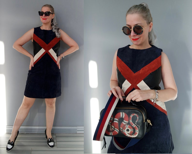 K&ouml;nnte beinhalten: &Auml;rmelloses marineblaues Kleid mit einem geometrischen Design in Rot, Schwarz und Wei&szlig;. Das Outfit umfasst schwarz-wei&szlig;e Schuhe und eine schwarze Handtasche mit Schlangenmuster und einem gestreiften Riemen. Das Model tr&auml;gt eine Sonnenbrille und ein Armband.