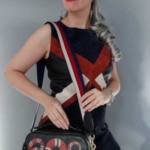 K&ouml;nnte beinhalten: Eine Frau tr&auml;gt eine runde Sonnenbrille mit Text, ein marineblaues und rotes Kleid und eine schwarze Umh&auml;ngetasche. Die Tasche hat ein rotes und wei&szlig;es Schlangenmuster. Der Riemen ist rot, wei&szlig; und blau gestreift.