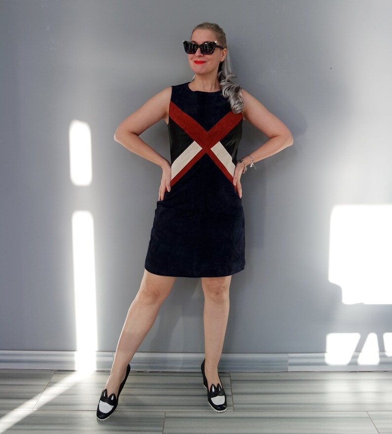K&ouml;nnte beinhalten: Ein &auml;rmelloses marineblaues Kleid mit einem geometrischen Design in Rot, Schwarz und Creme. Das Kleid ist knielang und hat eine taillierte Silhouette. Die Person tr&auml;gt schwarz-wei&szlig;e Loafer mit Katzenmotiv und Sonnenbrille.