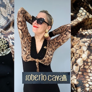 Könnte beinhalten: Ein schwarzes Kleid mit einem Bolero mit Schlangenmuster. Der Bolero hat lange Ärmel und ein braunes und beiges Muster. Das Kleid hat eine goldfarbene Brosche und das Etikett "roberto cavalli" in goldfarbenen Buchstaben.