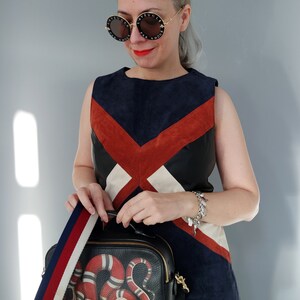 K&ouml;nnte beinhalten: Eine Frau tr&auml;gt ein farbblockiertes Kleid und runde Sonnenbrillen. Sie tr&auml;gt eine schwarze Lederhandtasche mit einem rot-wei&szlig;en Schlangenmuster und einem gestreiften Riemen. Die Sonnenbrille hat Text um die Gl&auml;ser.