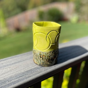 May include: A yellow ceramic mug with a geometric pattern. The mug has a textured, mosaic-like design on the bottom half.