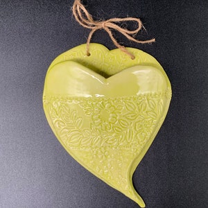 May include: A green ceramic heart-shaped planter with a floral design and a twine hanger.
