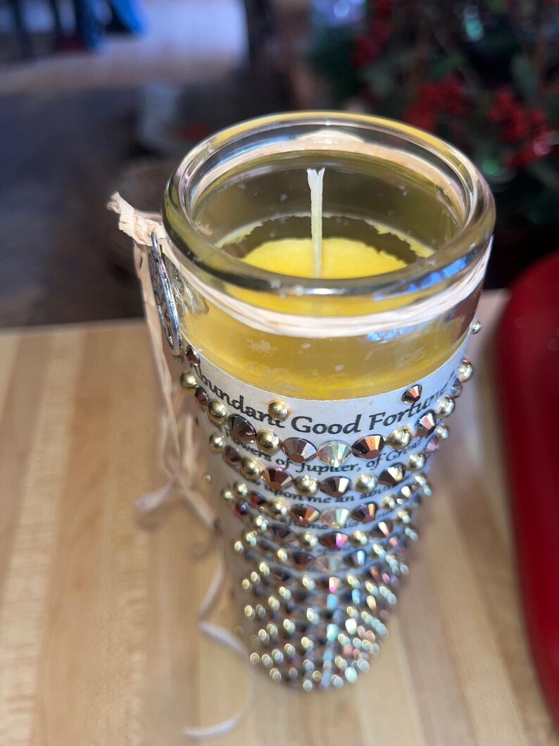 K&ouml;nnte beinhalten: Ein klares Glasgef&auml;&szlig; mit einer gelben Kerze darin. Das Gef&auml;&szlig; ist mit goldenen Strasssteinen verziert und tr&auml;gt ein Etikett mit der Aufschrift "Abundant Good Fortune, Powers of Jupiter, of Greatness, bestow upon me an abundance of..."