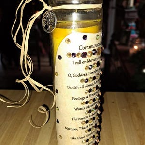 May include: A yellow candle with a label that reads "Communication Spell". The label has a list of words and phrases related to communication, including "Banish all silence", "Feelings & Freedom", "Words into actions", and "The need to be heard".